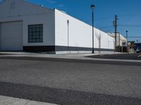 a empty street near a warehouse building and power lines in the background with blue skies