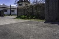 a view from across an open driveway onto an empty street and a church tower and the outside, with bare grass, shrubs,