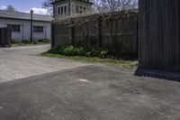 a view from across an open driveway onto an empty street and a church tower and the outside, with bare grass, shrubs,