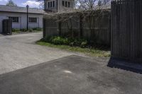 a view from across an open driveway onto an empty street and a church tower and the outside, with bare grass, shrubs,