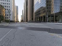 the empty street has an asphalt sidewalk with a hole in the middle, along with tall buildings