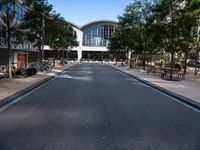 an empty street with parked motorcycles and trees near by a large building with a balcony