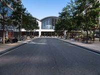 an empty street with parked motorcycles and trees near by a large building with a balcony