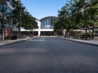 an empty street with parked motorcycles and trees near by a large building with a balcony