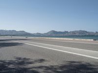 an empty street next to the ocean and mountains with a person walking on the road