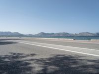 an empty street next to the ocean and mountains with a person walking on the road