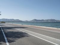 an empty street next to the ocean and mountains with a person walking on the road