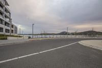 an empty street next to a parking lot near tall buildings and a fenced off area