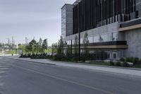 an empty street with concrete buildings along it and tall trees in the background on a hazy day