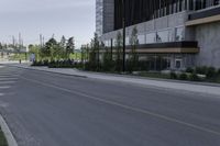 an empty street with concrete buildings along it and tall trees in the background on a hazy day