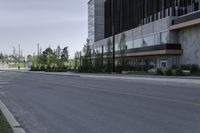 an empty street with concrete buildings along it and tall trees in the background on a hazy day