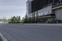 an empty street with concrete buildings along it and tall trees in the background on a hazy day