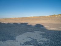 a view of an empty street with shadow of two people on the side of the road