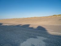 a view of an empty street with shadow of two people on the side of the road