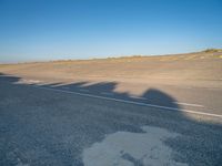 a view of an empty street with shadow of two people on the side of the road