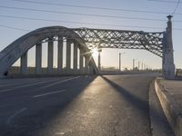 an empty street with the sun coming through the bridge and power lines in the background