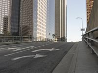 a view of the empty street with several arrows painted on it and tall buildings in the background