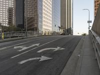 a view of the empty street with several arrows painted on it and tall buildings in the background