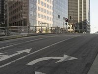 a view of the empty street with several arrows painted on it and tall buildings in the background