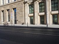 an empty street lined with tall stone buildings and trees in the background, next to parked bicycles