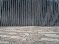 an empty street lined with gray bricks with a metal wall behind it in the background