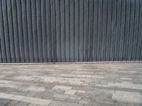 an empty street lined with gray bricks with a metal wall behind it in the background