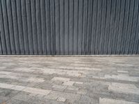 an empty street lined with gray bricks with a metal wall behind it in the background