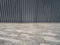 an empty street lined with gray bricks with a metal wall behind it in the background