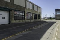 a empty street lined with industrial buildings in the background and a long yellow line in front of some of it's doors