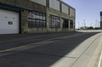 a empty street lined with industrial buildings in the background and a long yellow line in front of some of it's doors