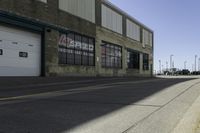 a empty street lined with industrial buildings in the background and a long yellow line in front of some of it's doors