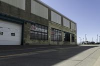 a empty street lined with industrial buildings in the background and a long yellow line in front of some of it's doors