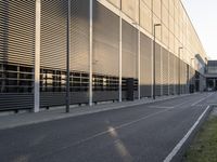 a man with a backpack rides on a skateboard along an empty street in front of an industrial building