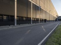 a man with a backpack rides on a skateboard along an empty street in front of an industrial building