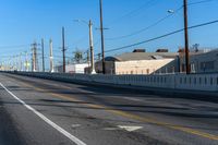 an empty street with lines on the sides of it and wires above the road, behind the fence, the buildings in the distance