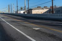 an empty street with lines on the sides of it and wires above the road, behind the fence, the buildings in the distance