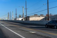 an empty street with lines on the sides of it and wires above the road, behind the fence, the buildings in the distance