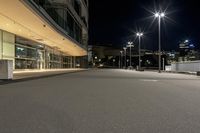the empty asphalted street is lit up by low light posts and lamps in the background