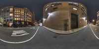 the street in front of buildings is empty at night time, as seen through two fish eye lenses