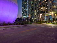 an empty street next to many tall buildings at night in the city, which is illuminated by a pink light