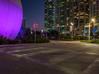 an empty street next to many tall buildings at night in the city, which is illuminated by a pink light