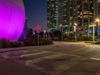 an empty street next to many tall buildings at night in the city, which is illuminated by a pink light