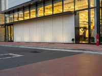 an empty street is seen behind a glass building near the intersection with an intersection sign