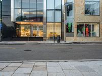 an empty street with store fronts along side a sidewalk that is partly shaded in by glass