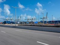 an empty street in front of cranes and shipyards near the water of a marina