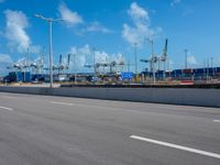 an empty street in front of cranes and shipyards near the water of a marina