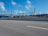 an empty street in front of cranes and shipyards near the water of a marina