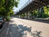 an empty street next to a bridge in a city with some people walking on the road