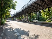 an empty street next to a bridge in a city with some people walking on the road