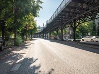 an empty street next to a bridge in a city with some people walking on the road